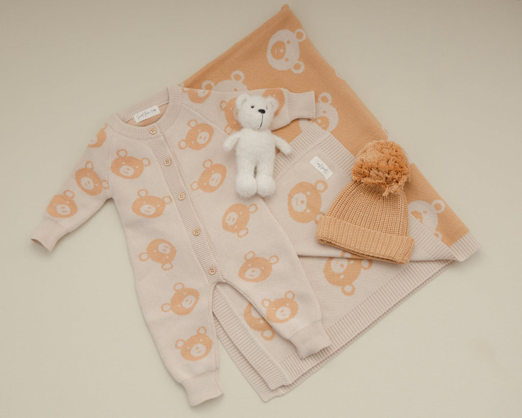 Baby outfit set with pink cardigan, beige pants, white teddy bear, and beige hat on a beige background sweet june