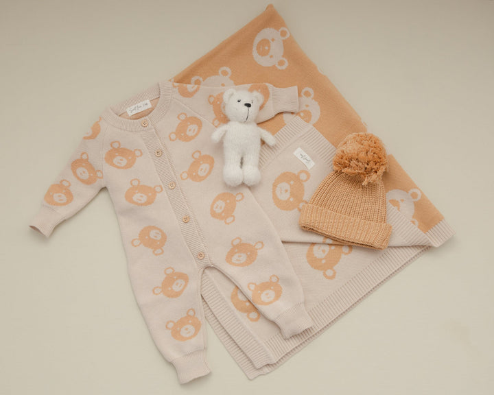 Baby outfit set with pink cardigan, beige pants, white teddy bear, and beige hat on a beige background sweet june