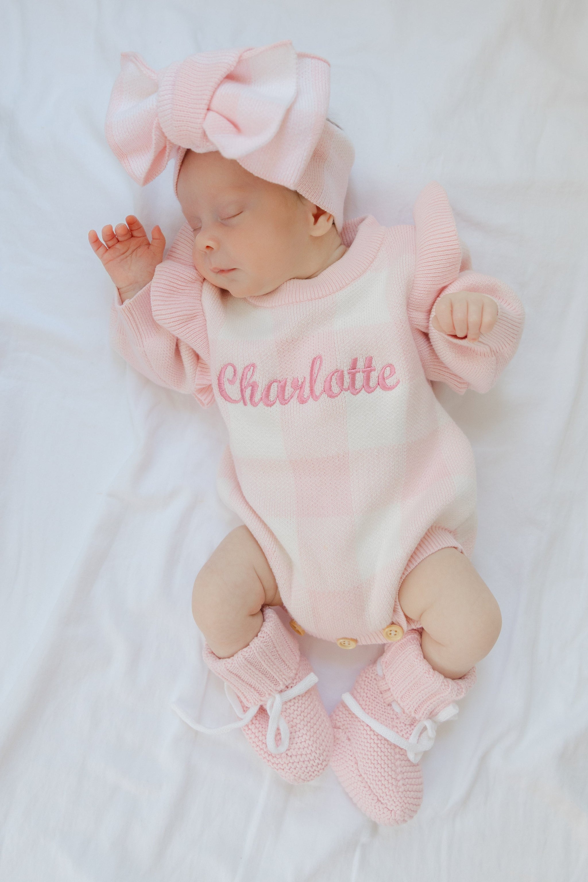 Newborn baby in pink outfit with 'Charlotte' on a white blanket sweet june